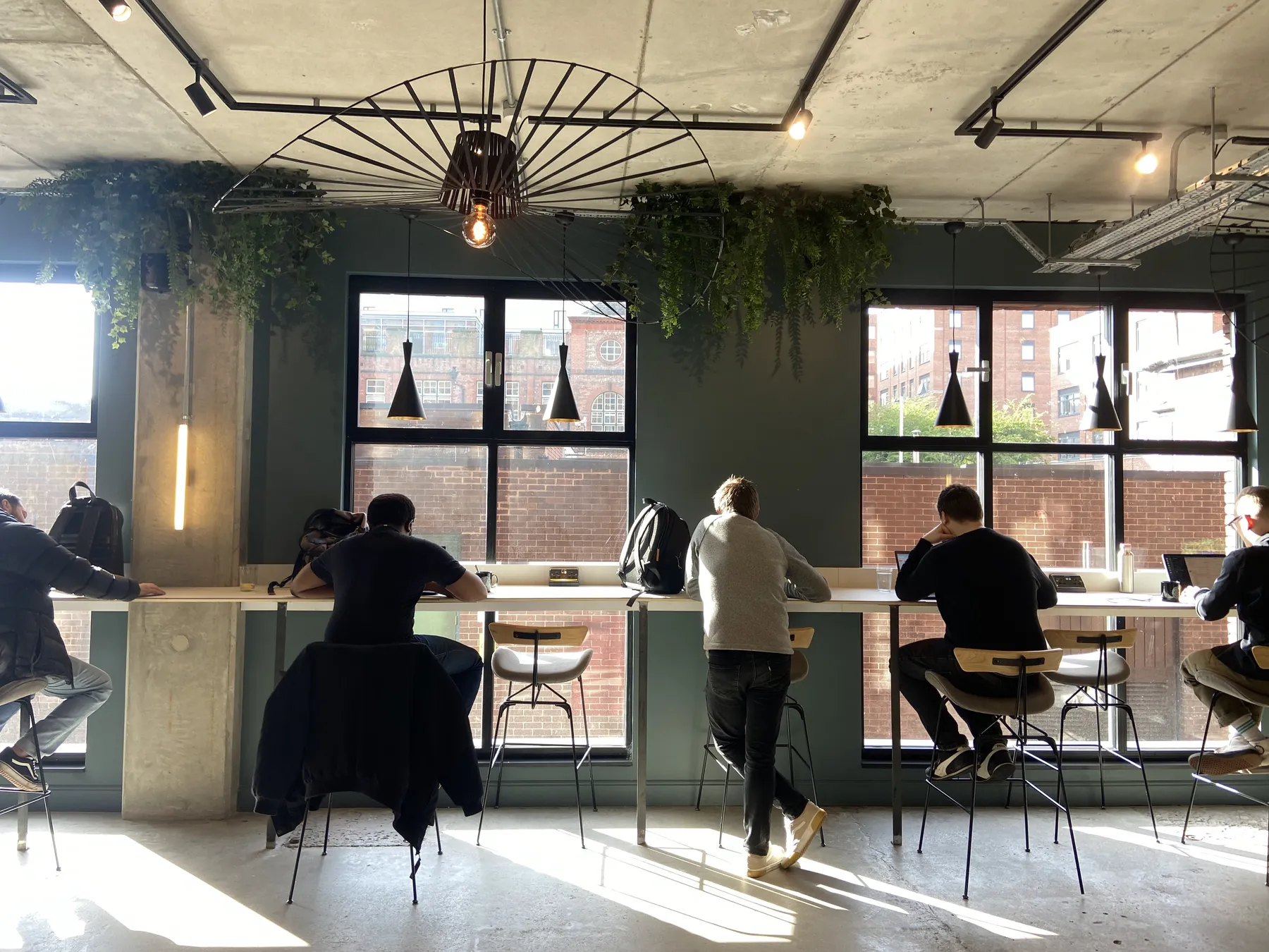 Colleagues working at a long window bench in a sunny co-working space in Manchester